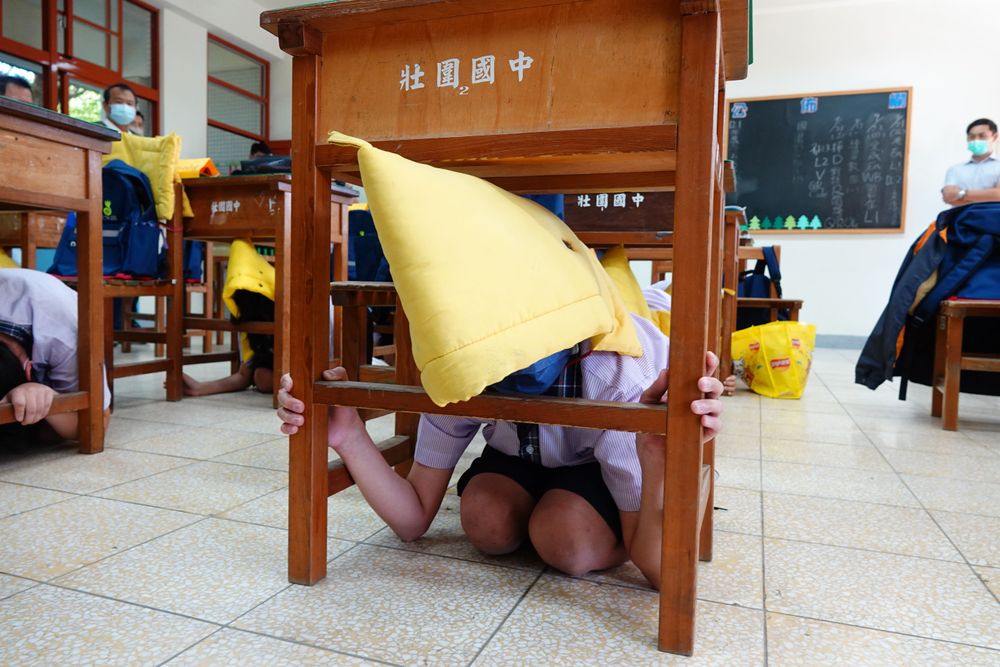 警報聲響起，學生戴起防災頭套躲在桌下避難。林泊志攝