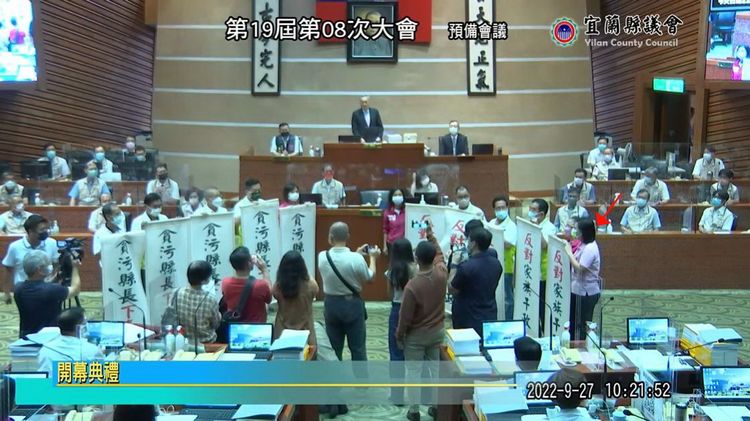 民進黨宜蘭縣議會黨團趁縣長林姿妙報告時舉「貪污縣長下臺」抗議，不過議會直播畫面中可清楚發現，民進黨宜蘭議員參選人黃惠慈（紅箭頭）也在場，遭批根本就是踐踏民意、藐視議會，把議會當成選舉秀場。翻攝宜蘭縣議會直播YT