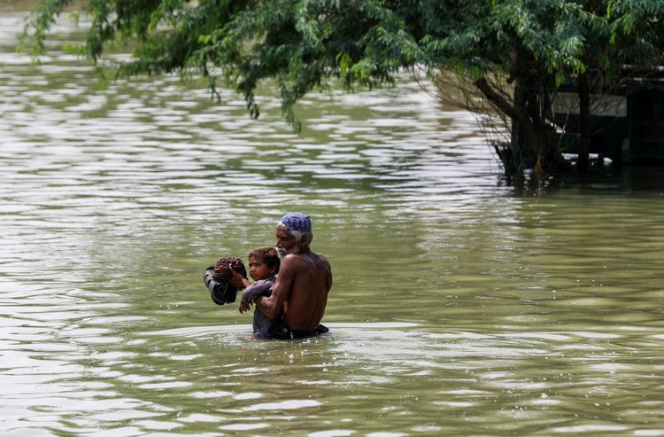 趁著雨勢停歇，災民抱著孩子在及腰積水之中涉水而過。路透社