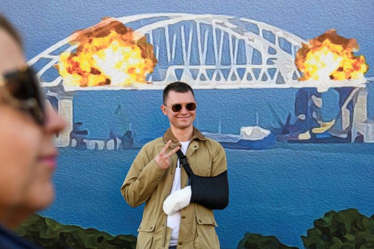 一名手臂受傷的男子，開心跟看板合照。路透社