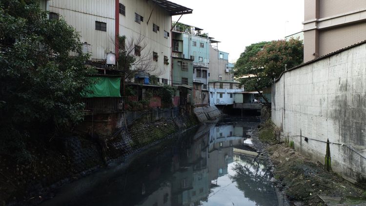 鴨母港溝上游整治前渠坡平緩環境髒臭。水利局提供