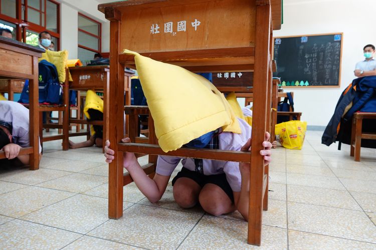 警報聲響起，學生戴起防災頭套躲在桌下避難。林泊志攝
