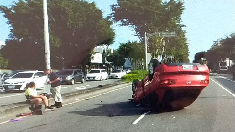 紅色自小客翻覆路中，陳姓女駕駛則自行爬出車外，坐在安全島等待送醫。讀者提供