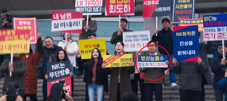 眼尖的網友發現劇中抗議的民眾舉著橫幅「輻射廢水崔道河全部喝下吧」（紅圈處），早已劇透崔道河的下場。翻攝Disney+